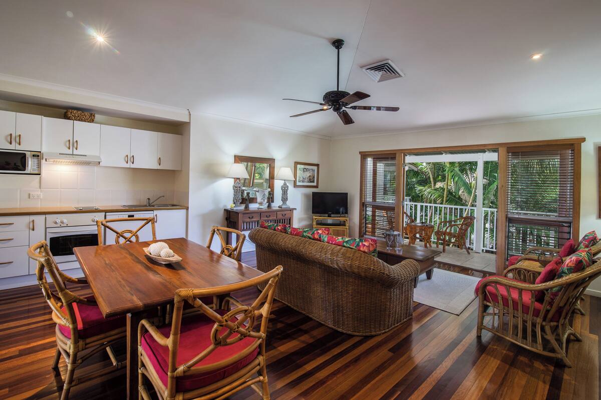 Un salón espacioso con una mesa de comedor de madera, mobiliario de mimbre y un televisor.