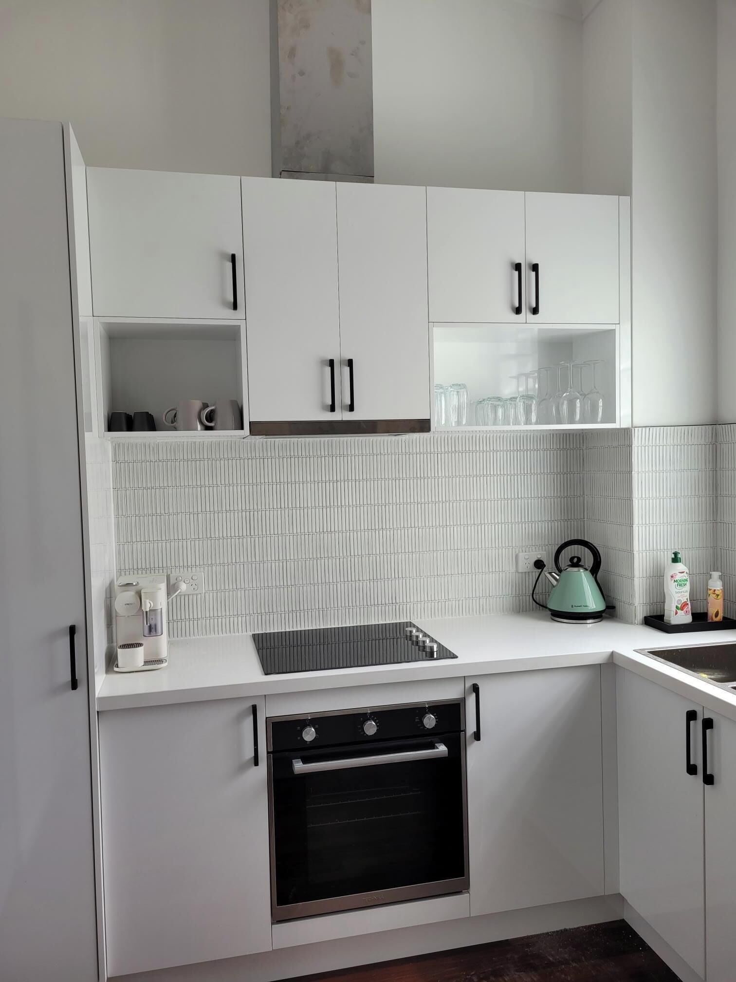 Una cocina moderna con armarios blancos, horno empotrado, cafetera y hervidor sobre la encimera.