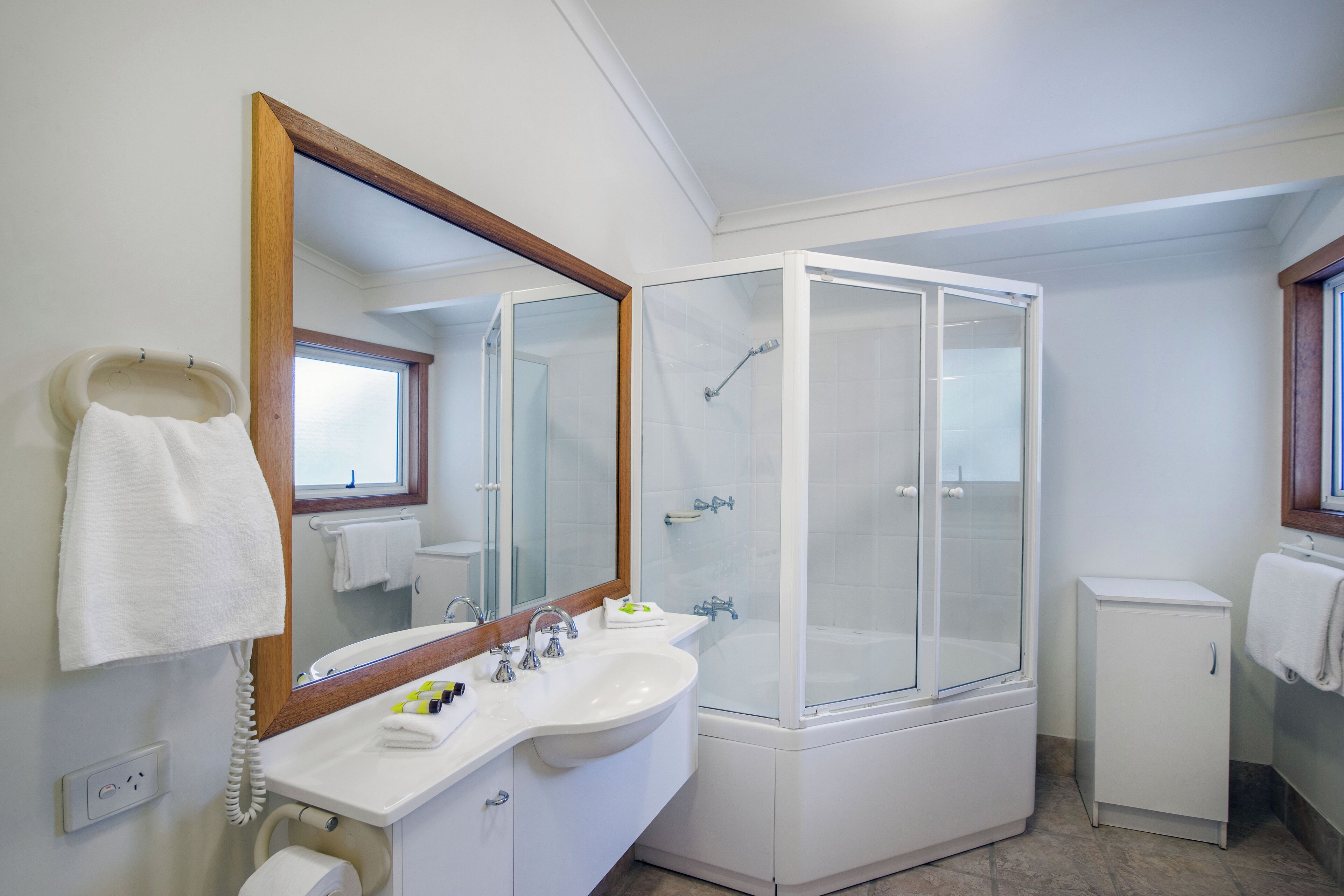 A bathroom with a sink, mirror, shower, and a small cabinet.