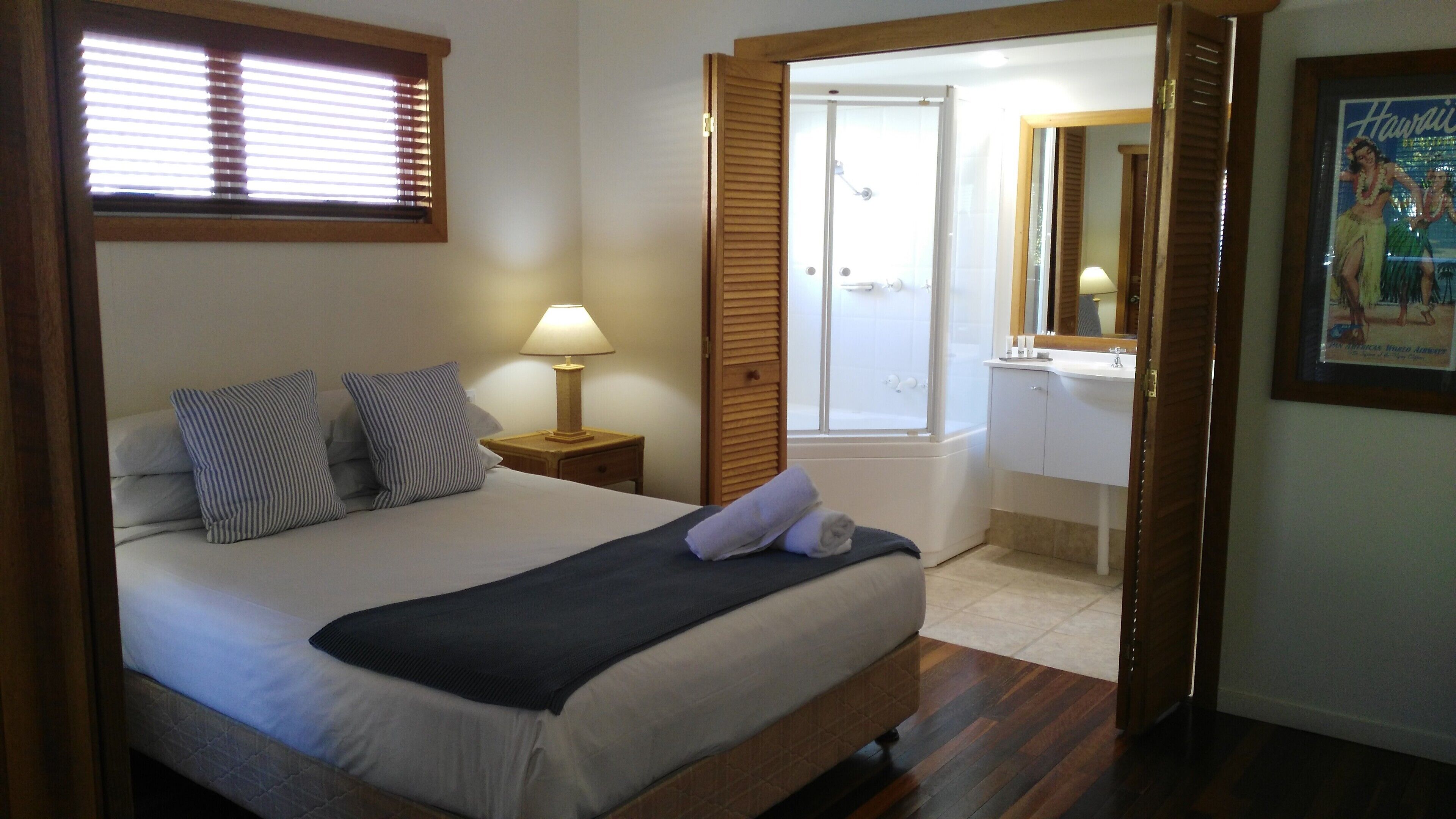 A hotel room with a bed, a nightstand, a lamp, a bathroom with a bathtub, and a framed picture on the wall.
