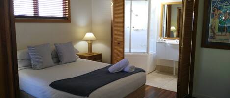 A hotel room with a bed, a nightstand, a lamp, a bathroom with a bathtub, and a framed picture on the wall.