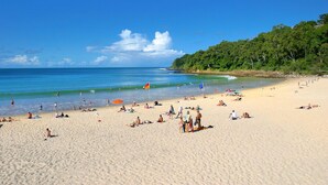Una playa con gente tomando el sol y nadando, una bandera y un cielo despejado.