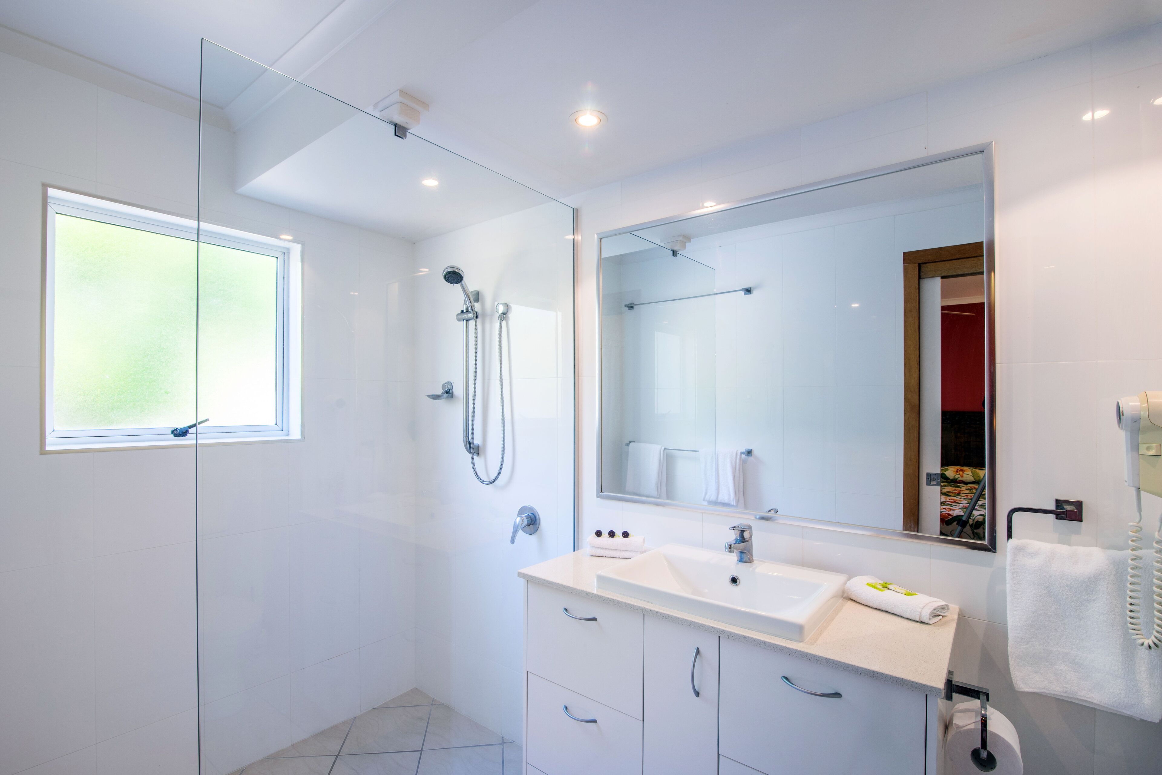 Une salle de bain moderne avec une douche à parois de verre, un grand miroir, un lavabo blanc et un porte-serviettes.