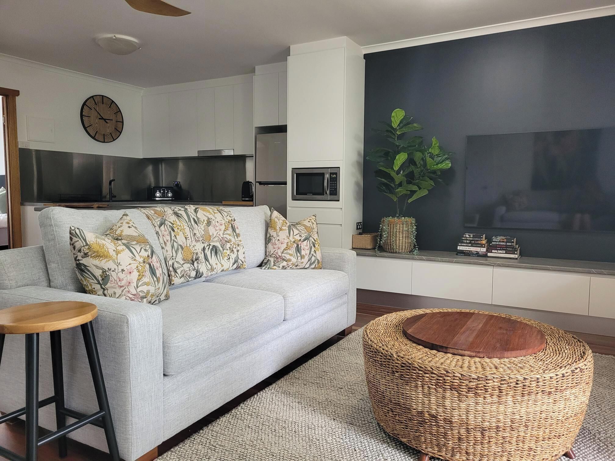 A modern living room with a grey sofa, a round woven coffee table, and a large window with a view of the outdoors.