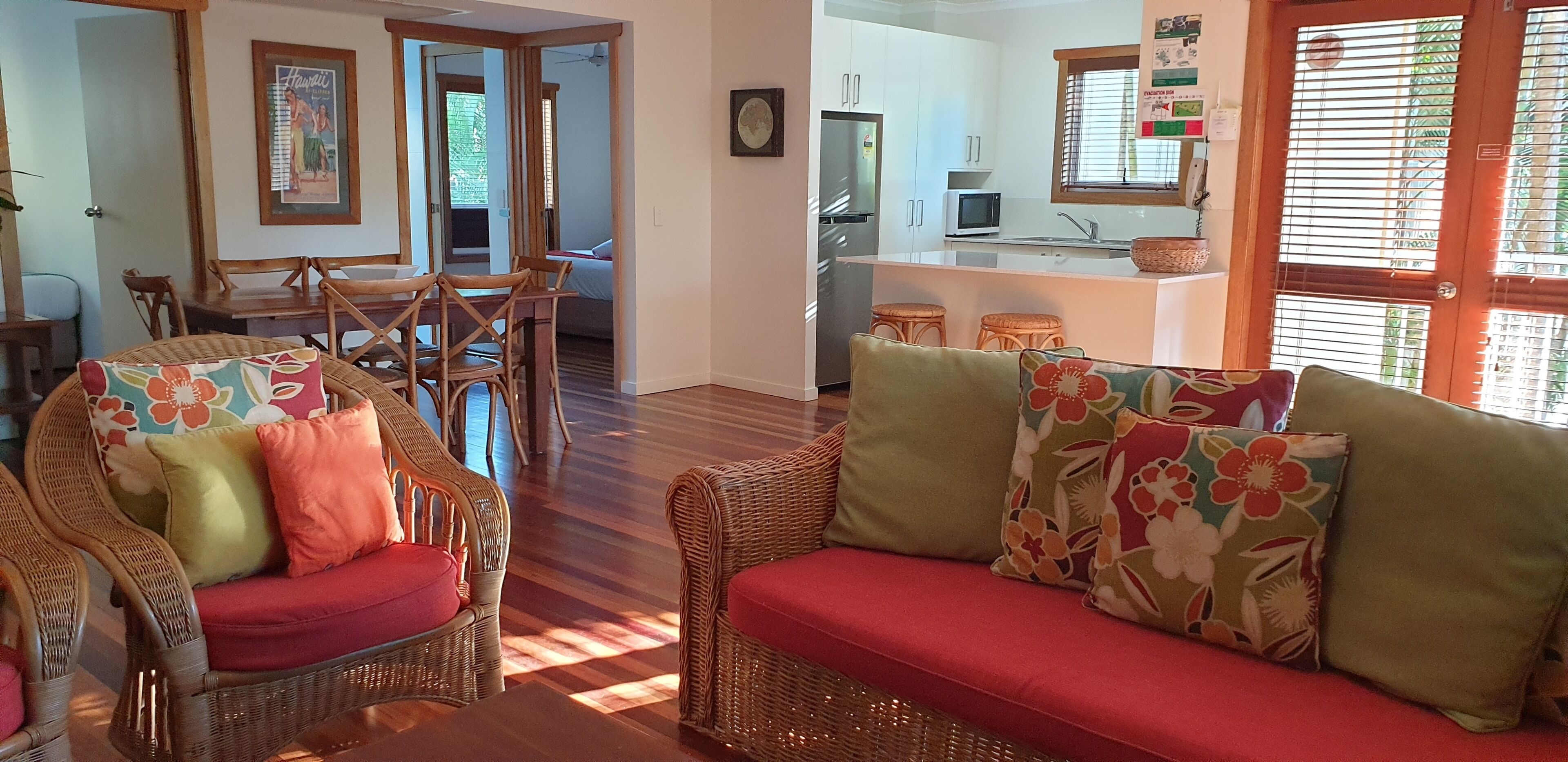 Una sala de estar acogedora con muebles de mimbre y cojines coloridos, un comedor con sillas de madera y una cocina con armarios blancos y un refrigerador.