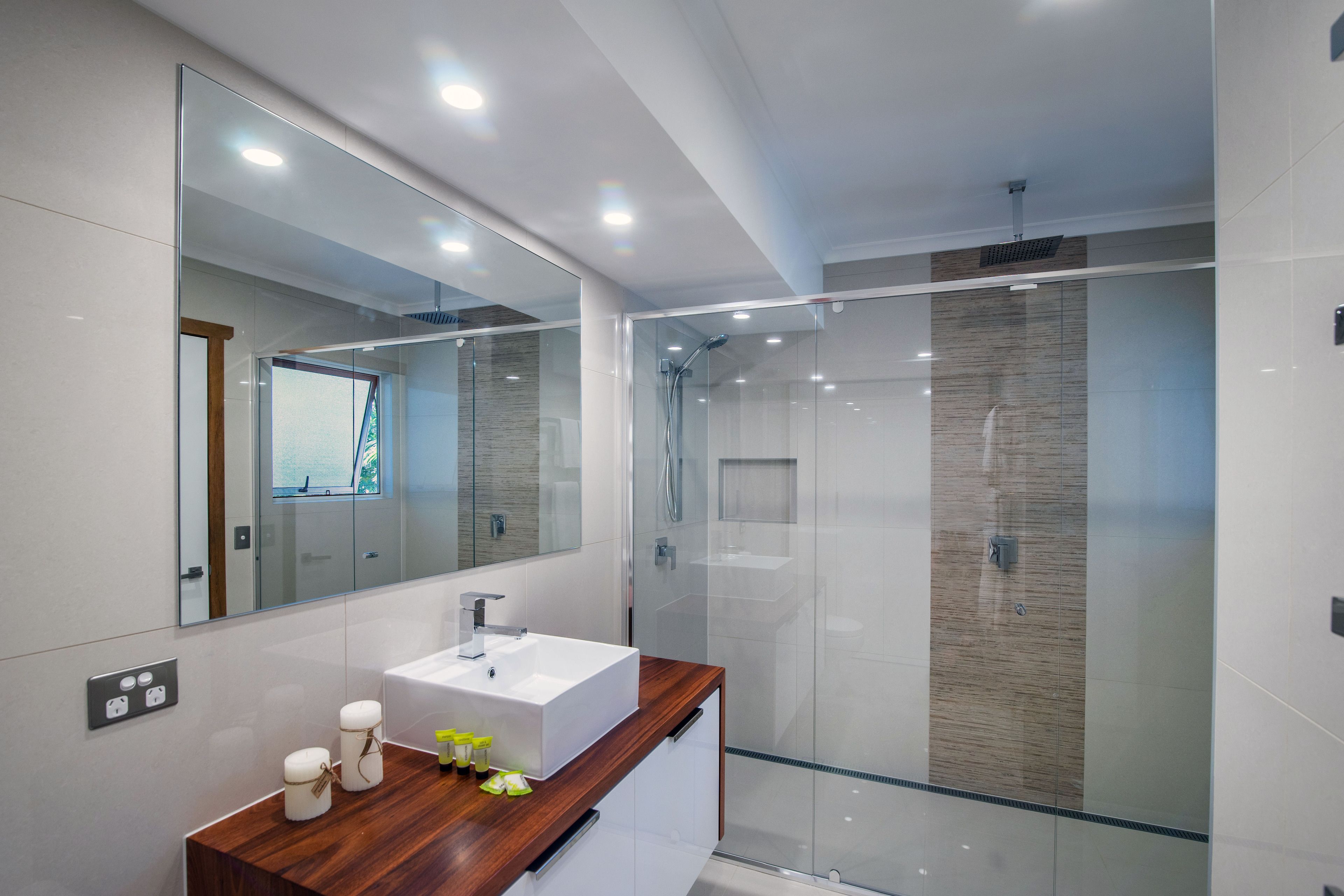 A modern bathroom with a glass shower enclosure, a wooden vanity, and a large mirror.