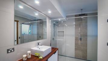 Un baño moderno con cabina de ducha de vidrio, tocador de madera y un espejo grande.