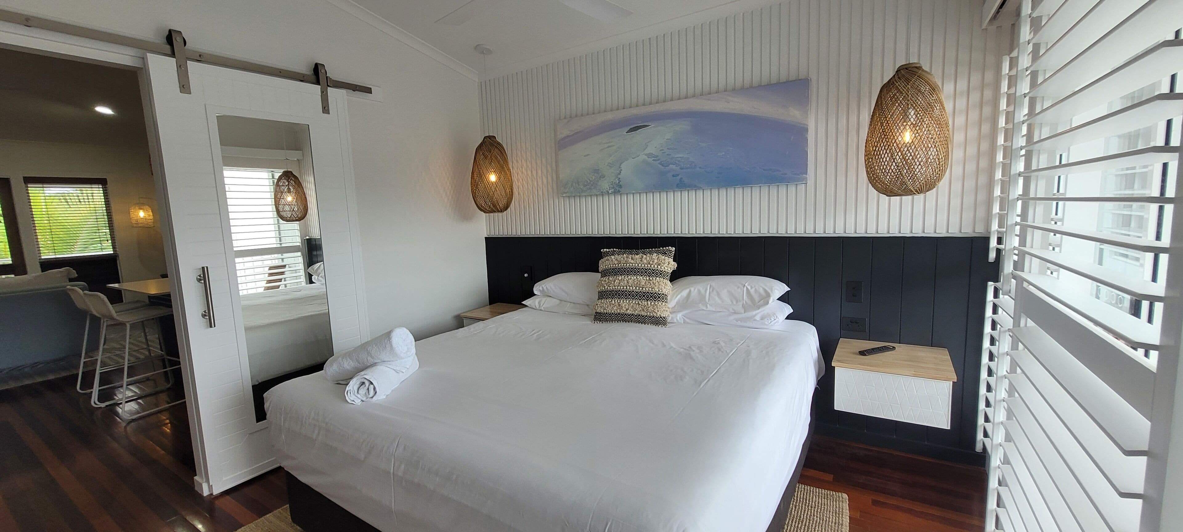 Een moderne hotelkamer met een groot bed, een schilderij aan de muur en uitzicht op zee.