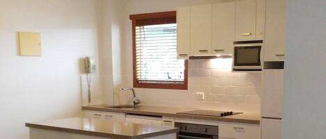 A compact kitchen with white cabinets, a built-in oven, and a microwave.