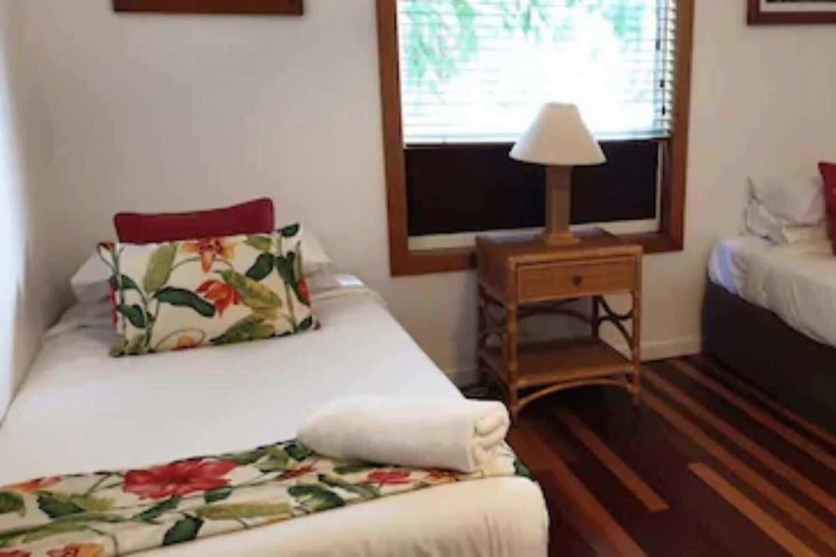 Una habitación con dos camas, una mesita de noche, una lámpara y una ventana.