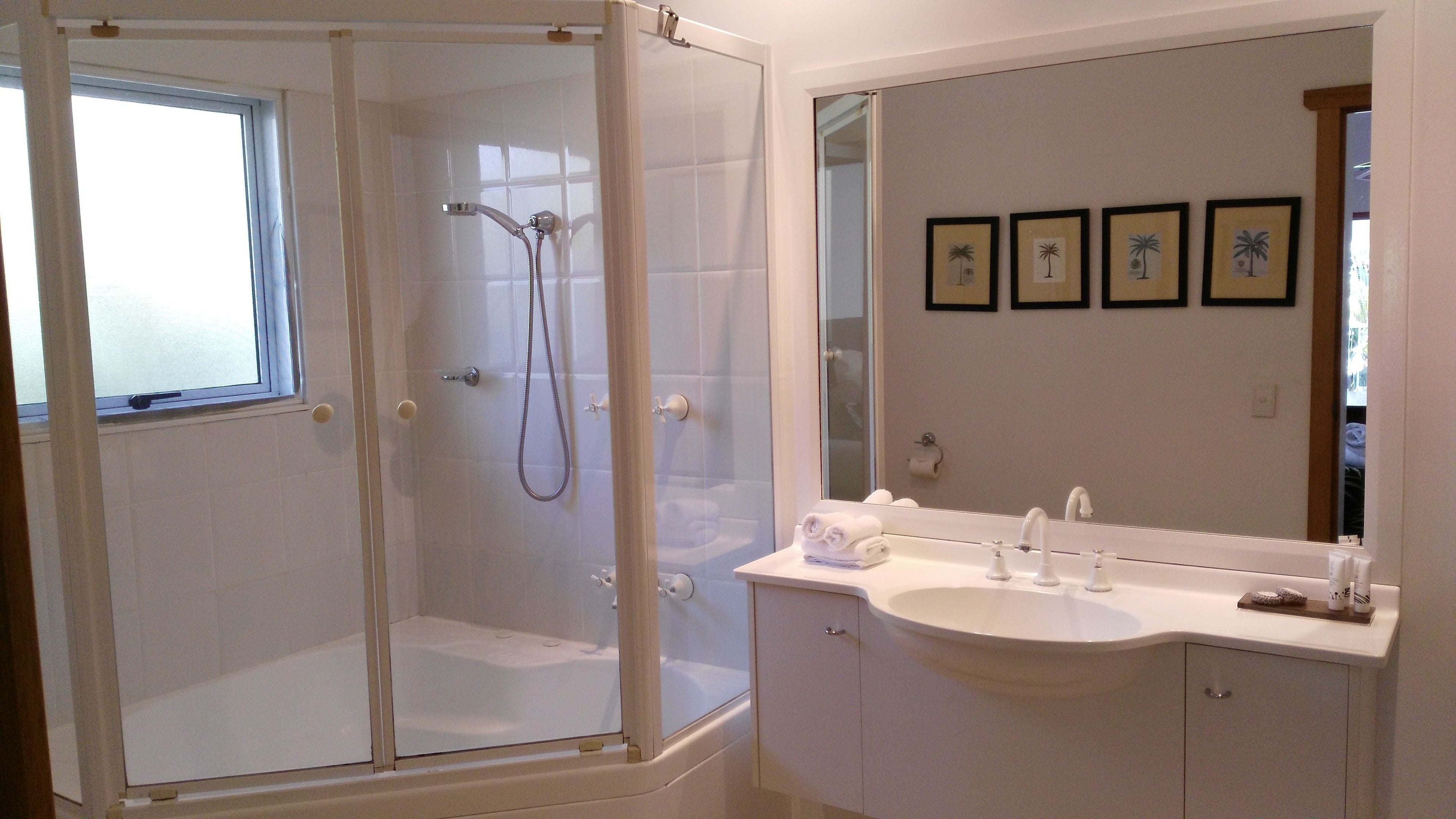 A bathroom with a glass-enclosed shower, a sink with a mirror, and framed pictures on the wall.