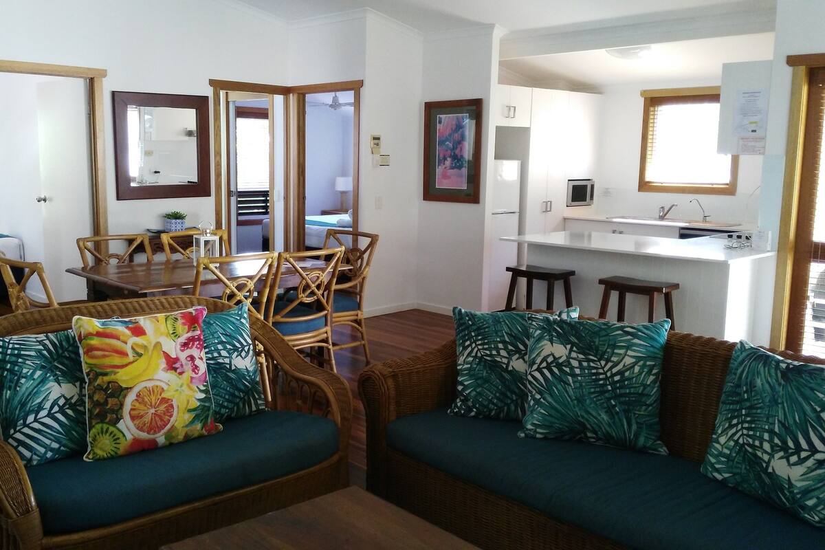 Una sala de estar acogedora con mobiliario de mimbre, una mesa de comedor y una kitchenette.