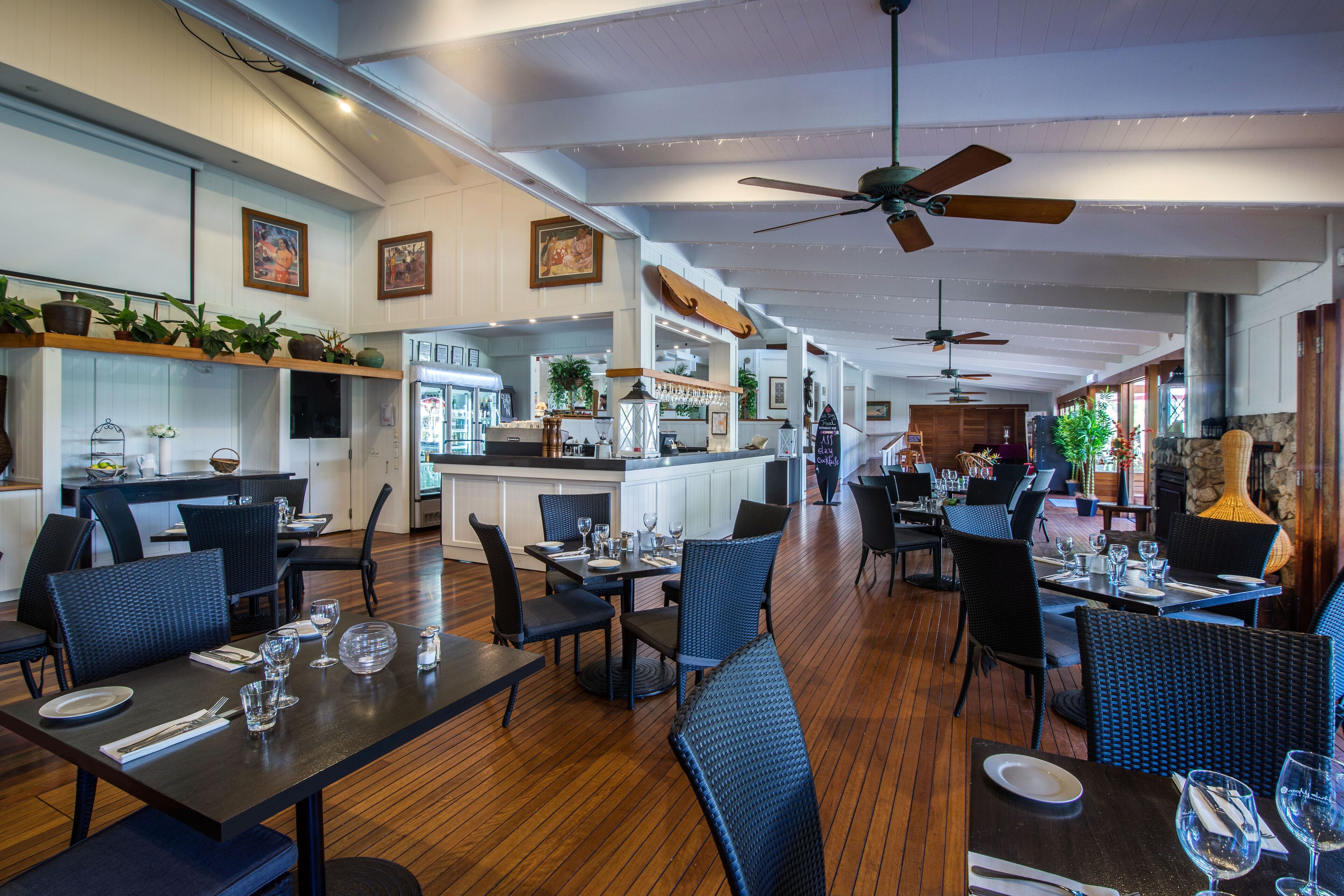 A restaurant with wooden flooring, black and blue upholstered chairs, and a bar area.