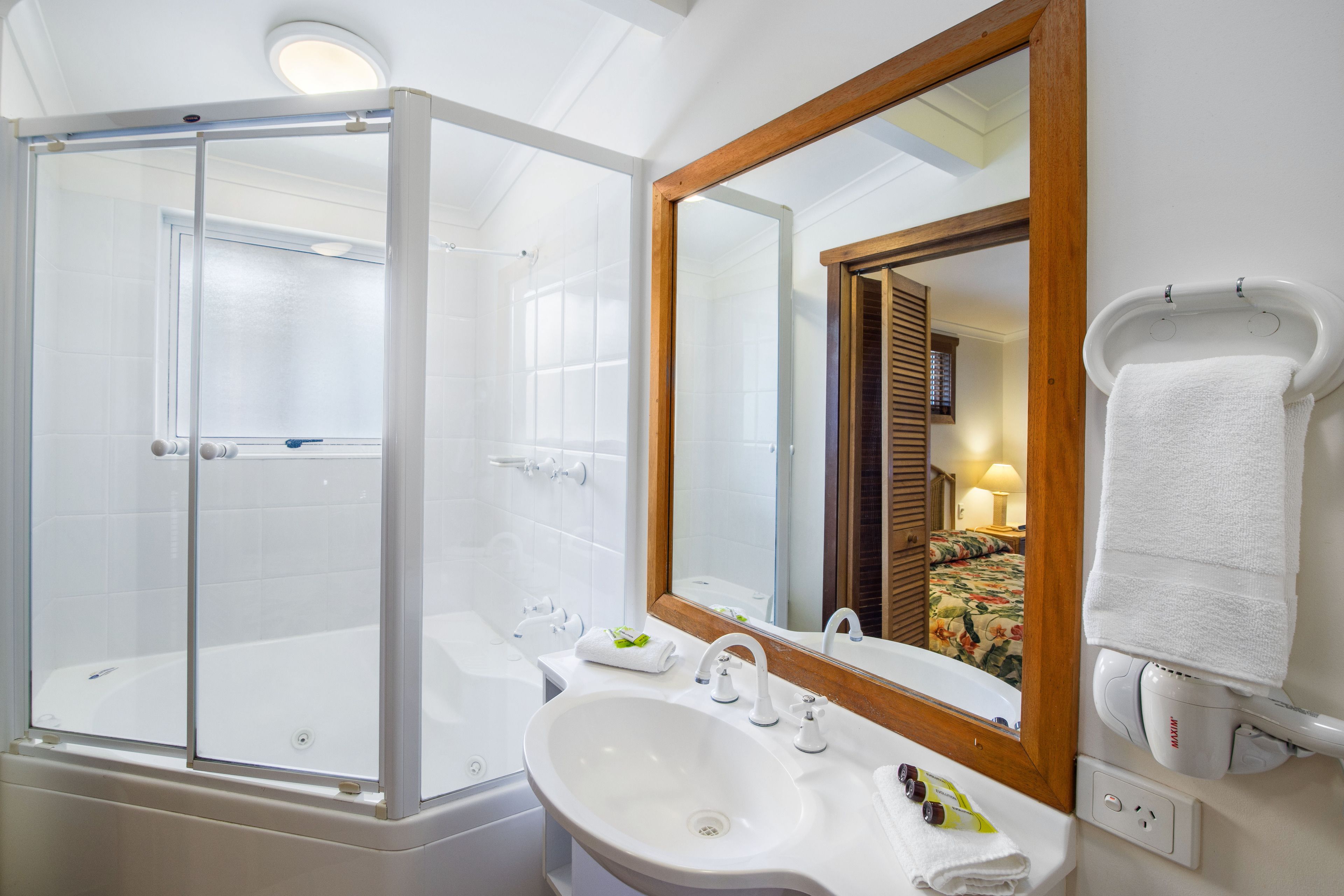 Un baño moderno con ducha de vidrio, un lavamanos grande y un espejo con marco de madera.