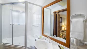 Un baño moderno con ducha de vidrio, un lavamanos grande y un espejo con marco de madera.