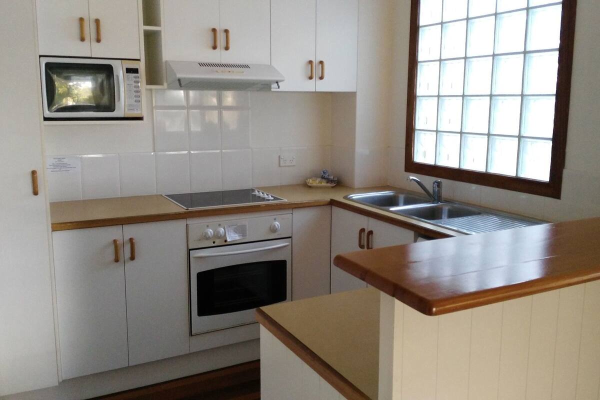 Una cocina con armarios blancos, un microondas, una estufa y una ventana con persianas.