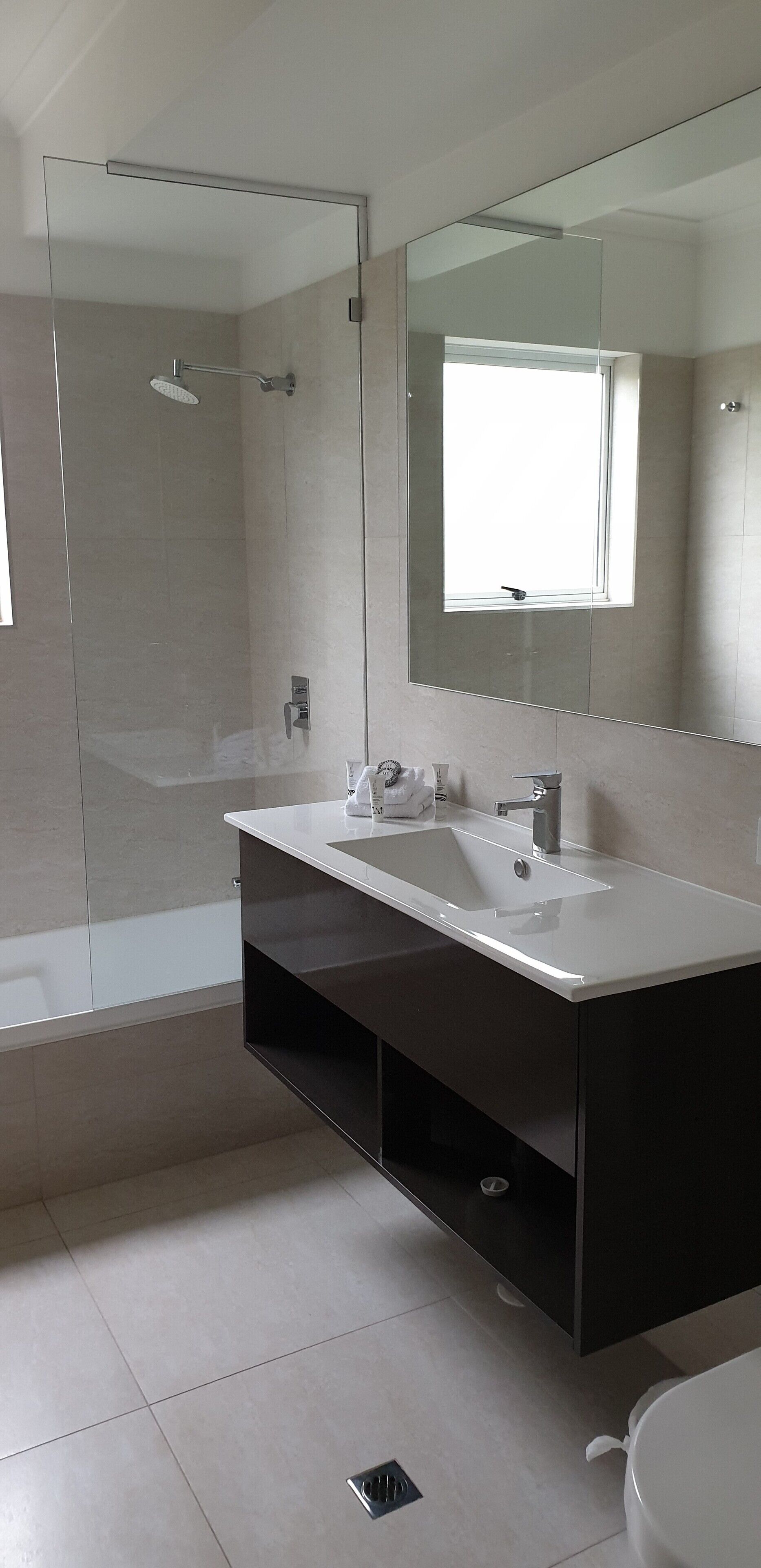 A modern bathroom with a glass-enclosed shower, a large mirror, and a white sink.
