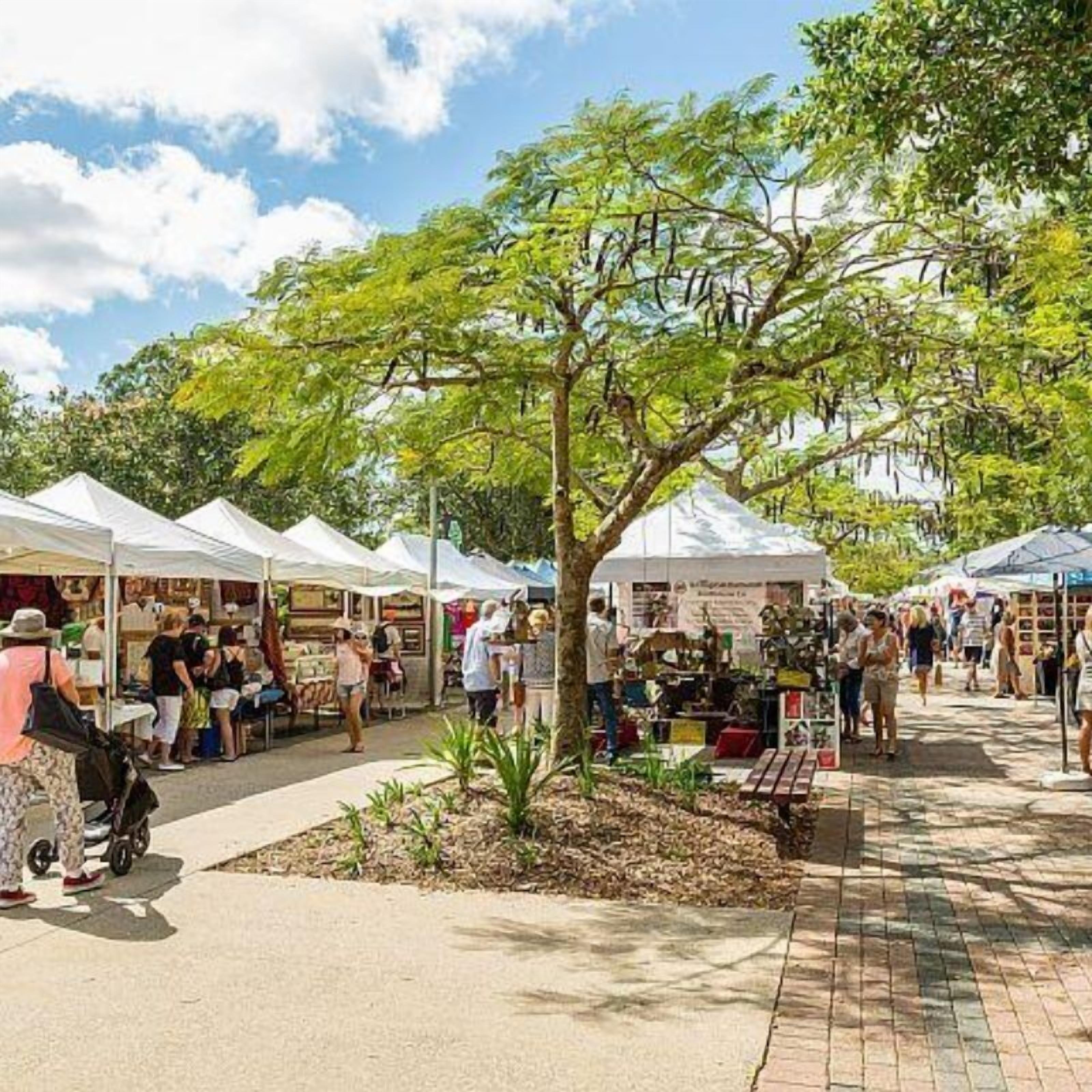Un mercado al aire libre con carpas blancas y gente mirando.
