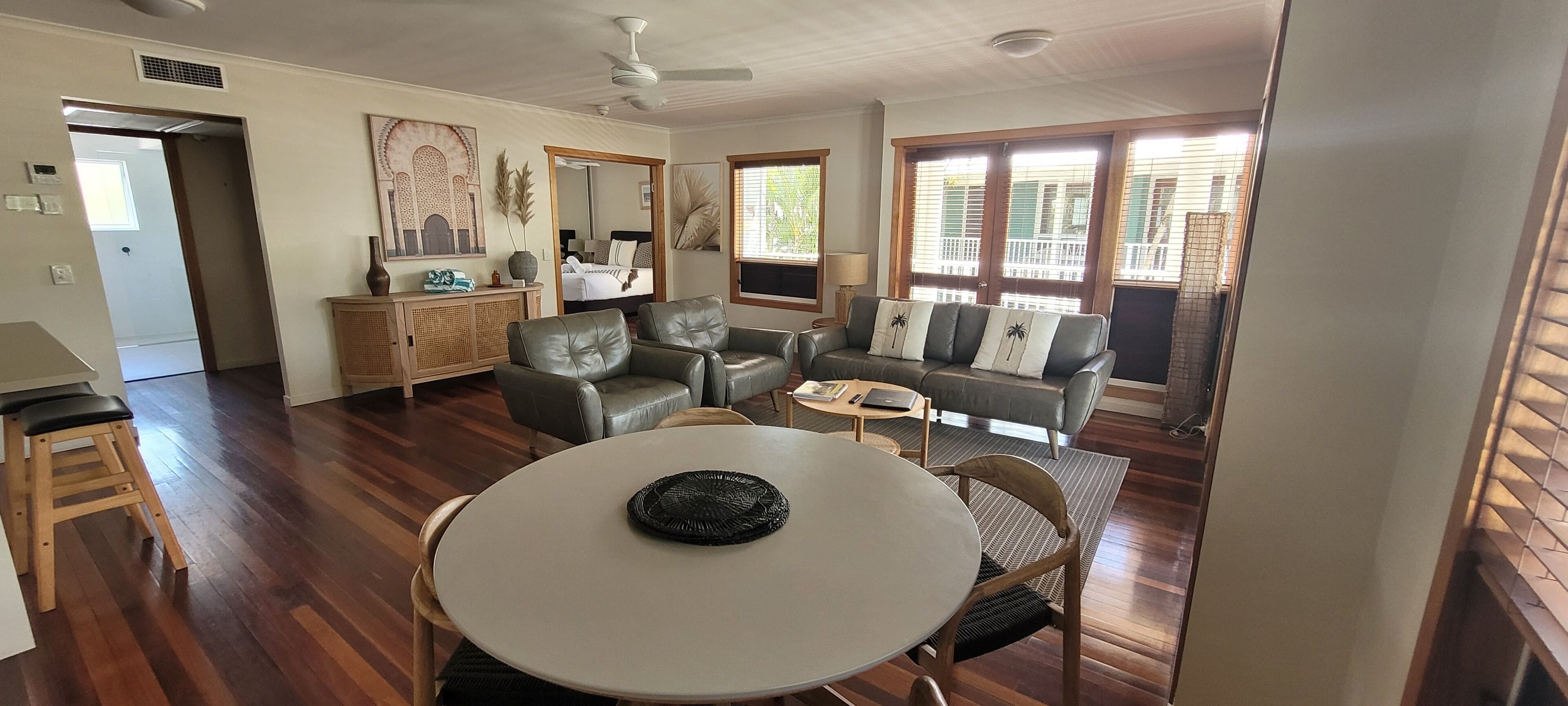 A spacious living room with a dining area, a sofa set, a coffee table, and a large window with blinds.