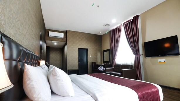 A hotel room with a large bed, a desk, a chair, a flat-screen TV, and a window with curtains. - Grand Kanaya Hotel (Medan)