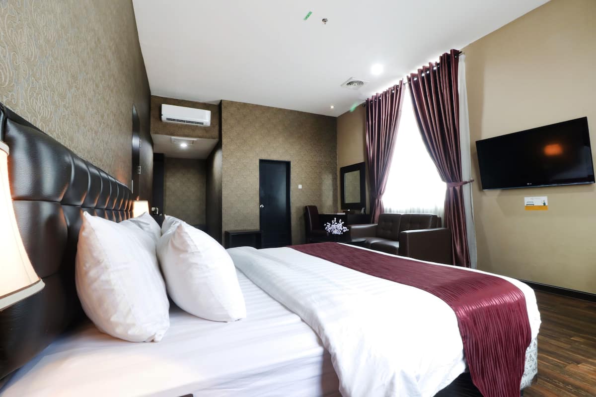 Quarto de hotel com uma cama grande, uma escrivaninha, uma cadeira, uma televisão de tela plana e uma janela com cortinas.