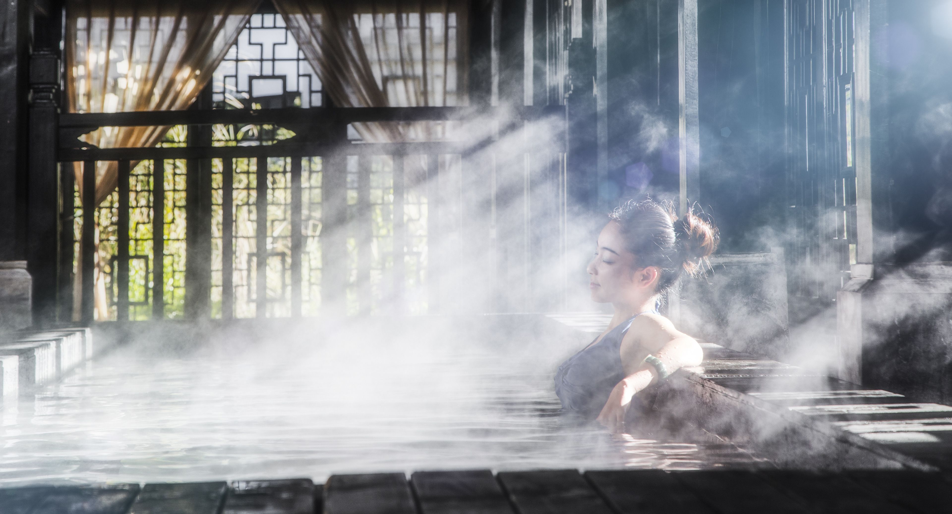 A person in a steam bath with a traditional wooden structure and a glass door in the background.