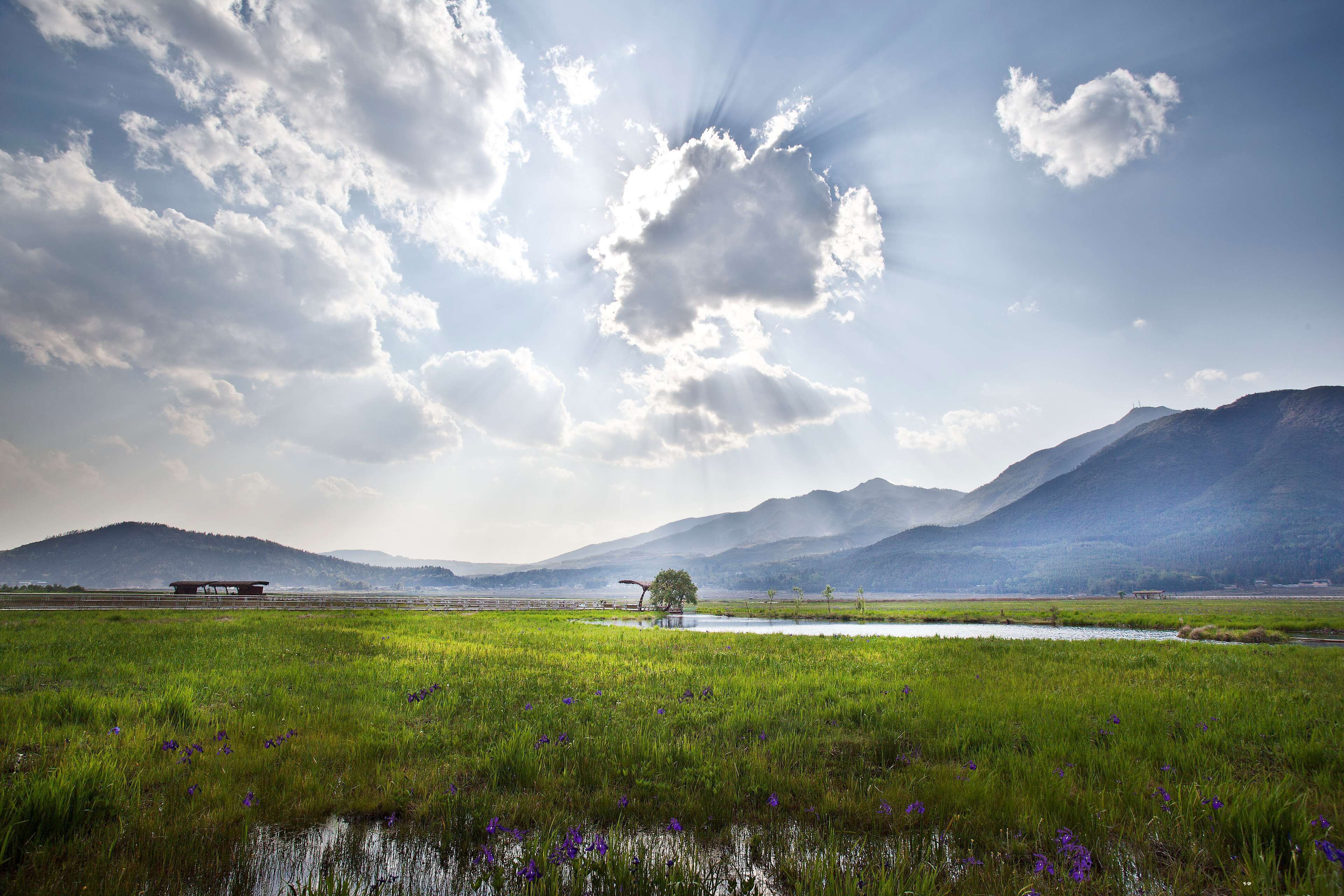 A landscape with a river, green fields, and mountains in the background.