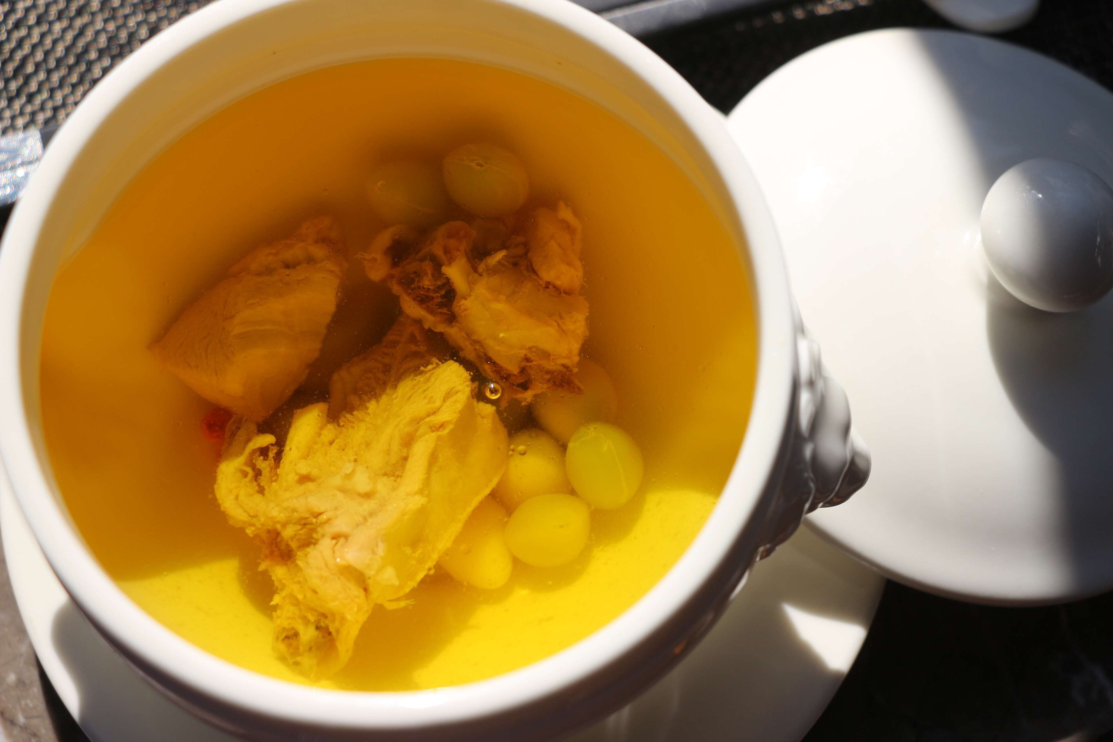 Una taza de cerámica blanca con un líquido amarillo y alimentos, incluyendo un trozo de pollo y esferas amarillas.
