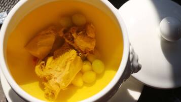 Una taza de cerámica blanca con un líquido amarillo y alimentos, incluyendo un trozo de pollo y esferas amarillas.