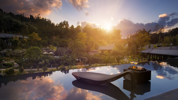 A serene outdoor setting with a reflective pool, traditional architecture, and lush greenery. - Banyan Tree Tengchong (Baoshan)