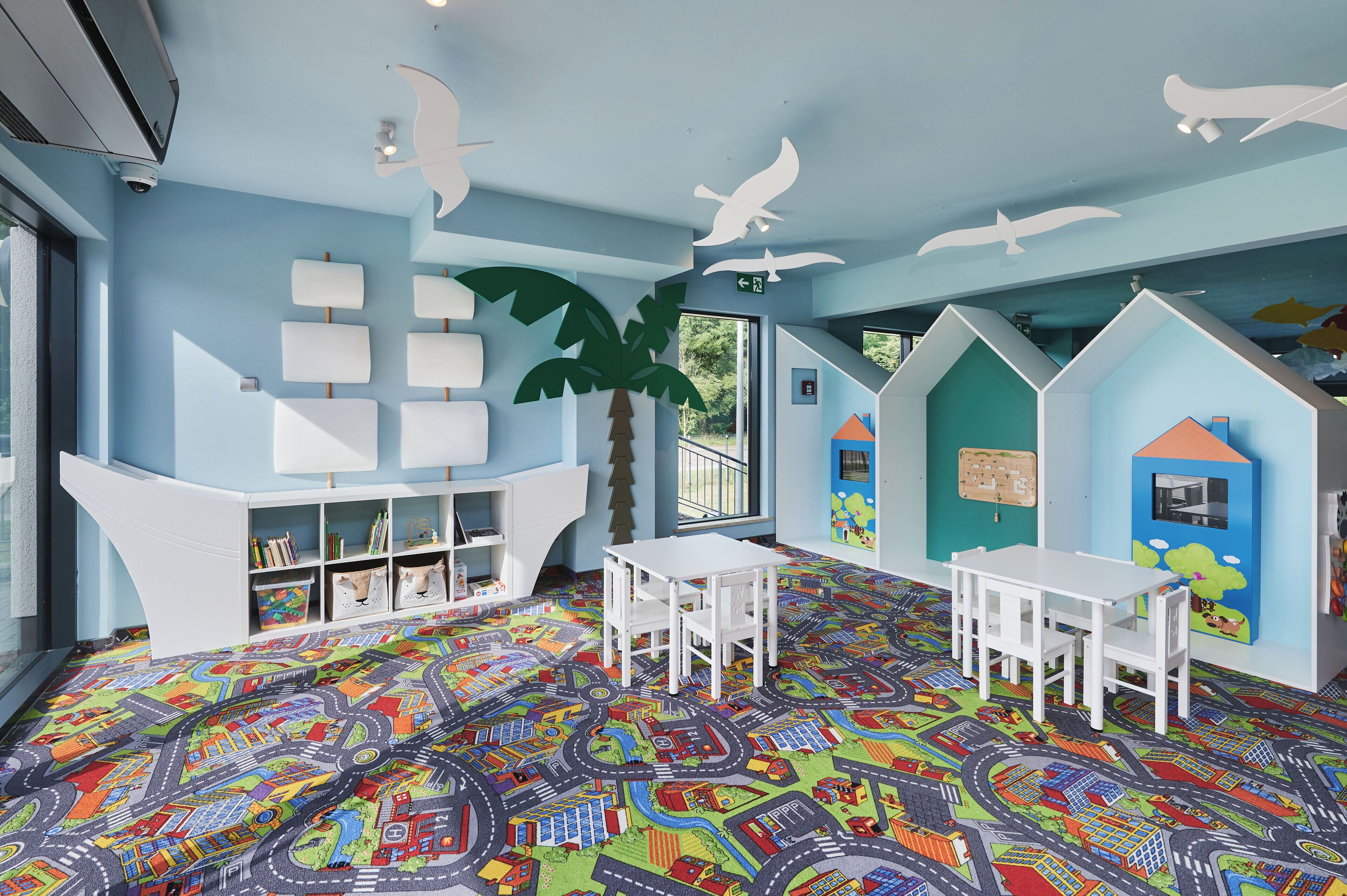 Una sala de juegos para niños con alfombra colorida, muebles blancos y decoraciones juguetonas en las paredes.