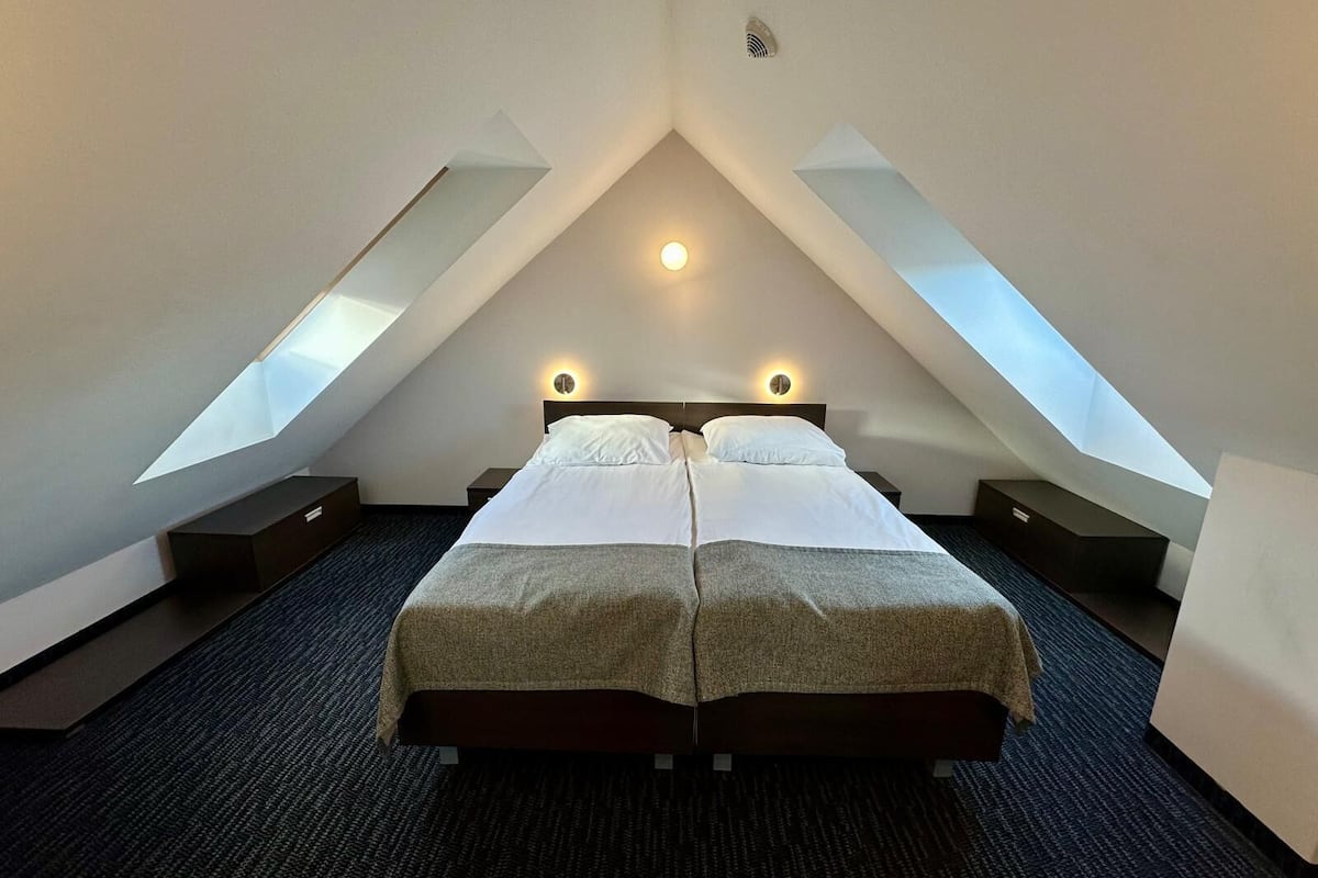 Ein modernes Hotelzimmer mit einem großen Bett, Dachfenstern und einem klaren, schlichten Design.