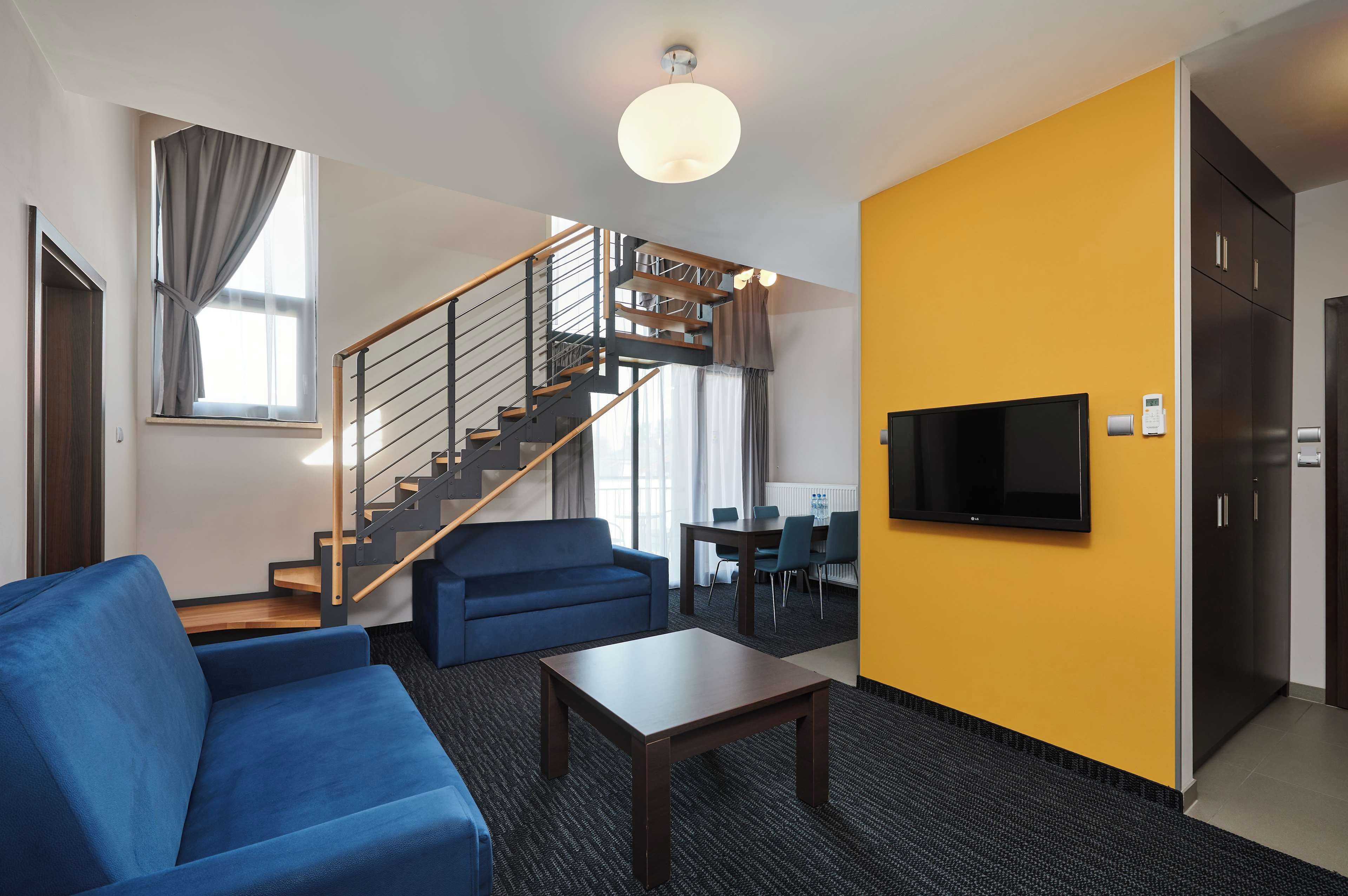 Habitación de hotel moderna con una escalera, un sofá, una mesa de centro y un televisor de pantalla plana.