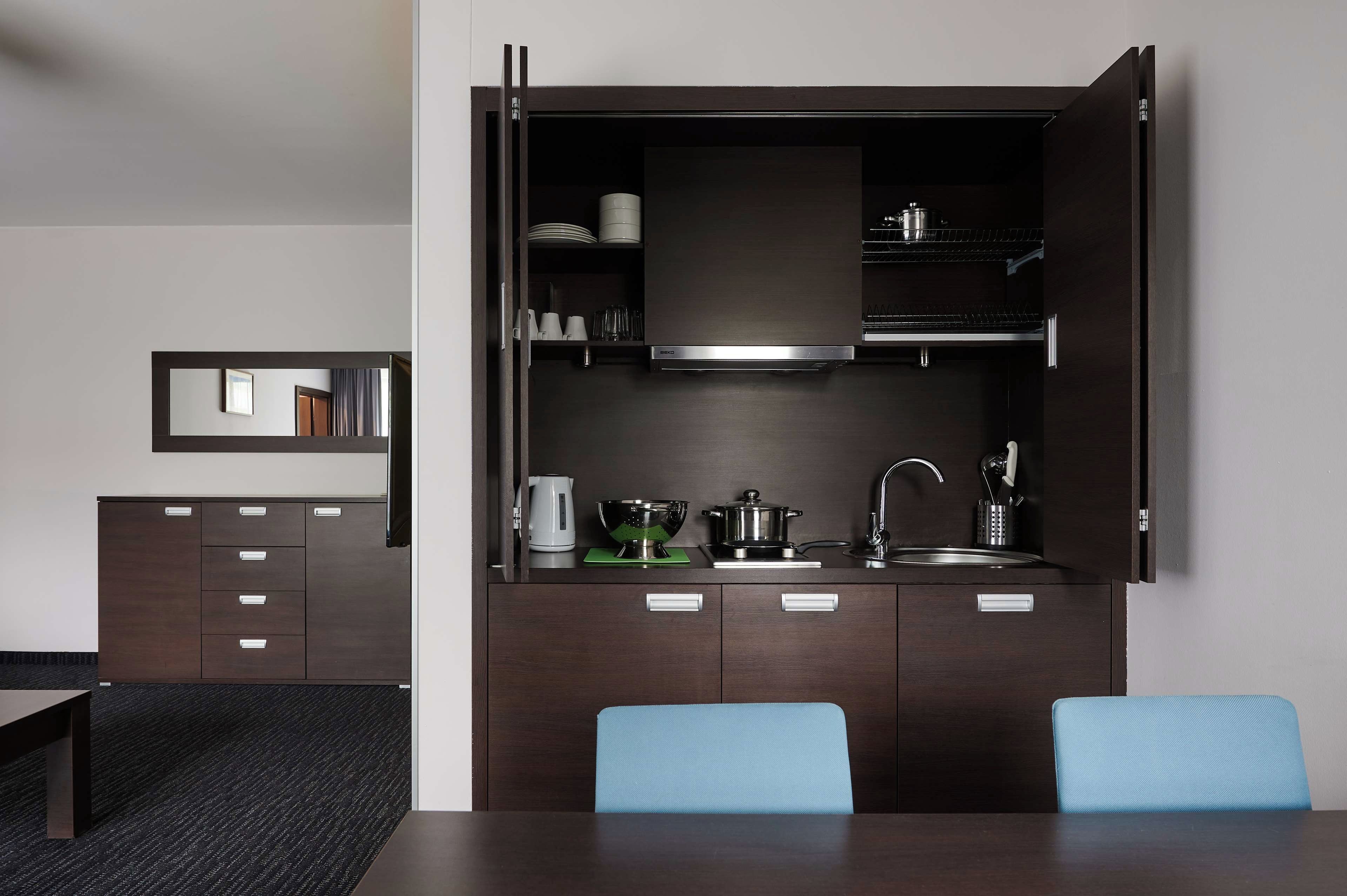 A compact kitchen with a built-in stove, a sink, and a microwave. There are two chairs and a small table in front.