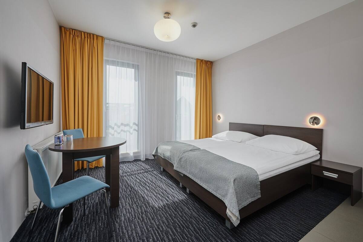 Ein Hotelzimmer mit Bett, Nachttisch, Stuhl und einem kleinen Tisch mit Lampe.