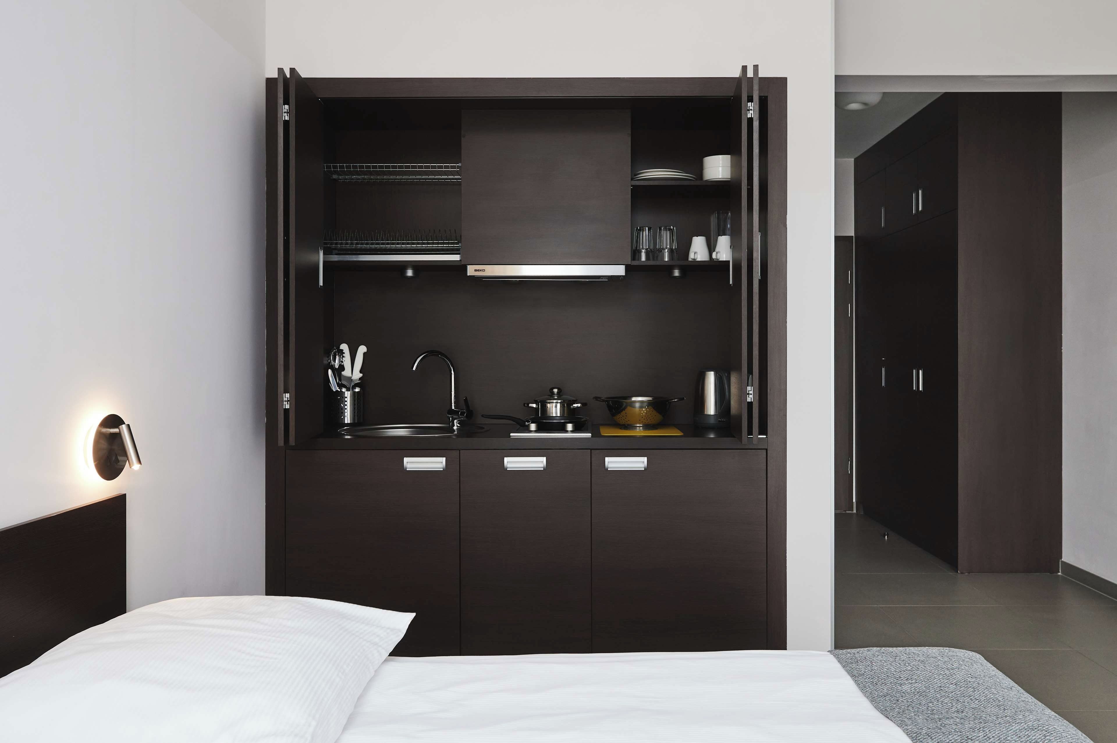 A modern bedroom with a built-in dark wood wardrobe, a bed with white linens, and a wall-mounted light fixture.