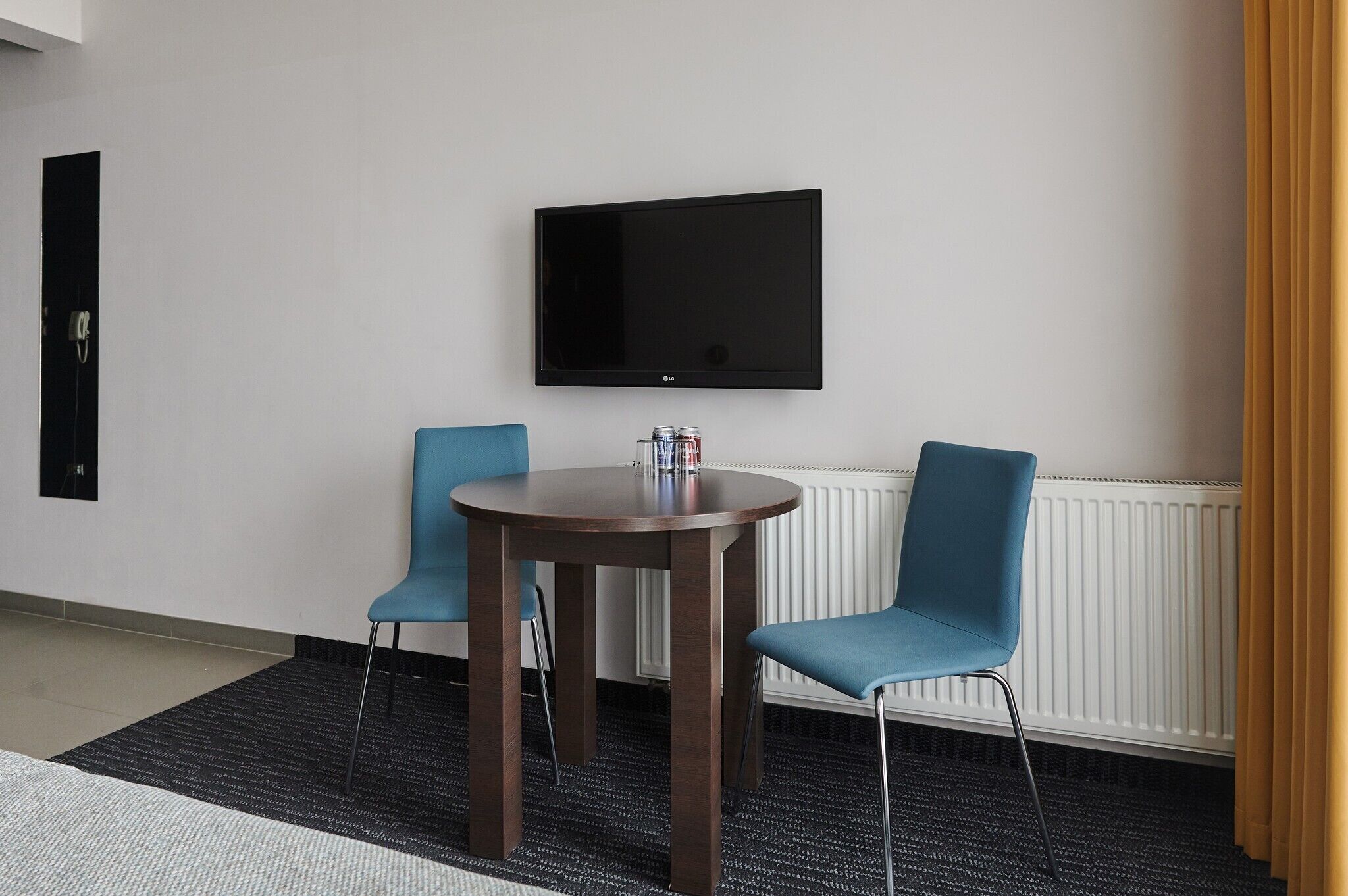 Ein Zimmer mit einem runden Holztisch, zwei blauen Stühlen, einem Flachbildfernseher an der Wand und einer Heizung.