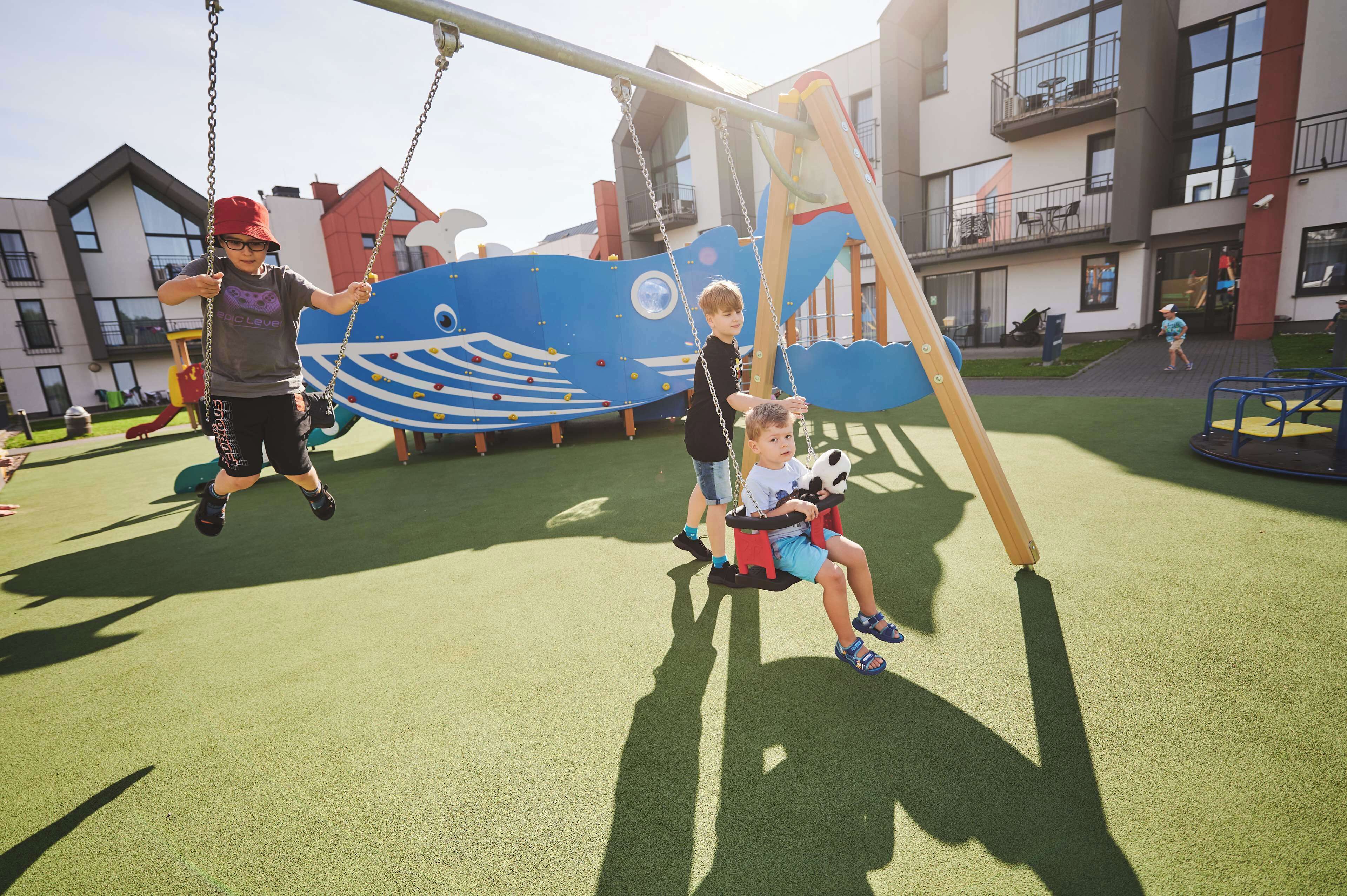 A playground with swings and a slide, surrounded by buildings.