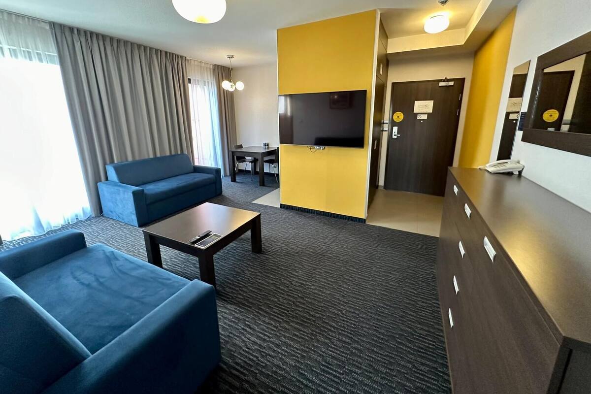 Ein Hotelzimmer mit Sofa, einem kleinen Tisch, einem Fernseher und einem Schreibtisch mit Telefon.