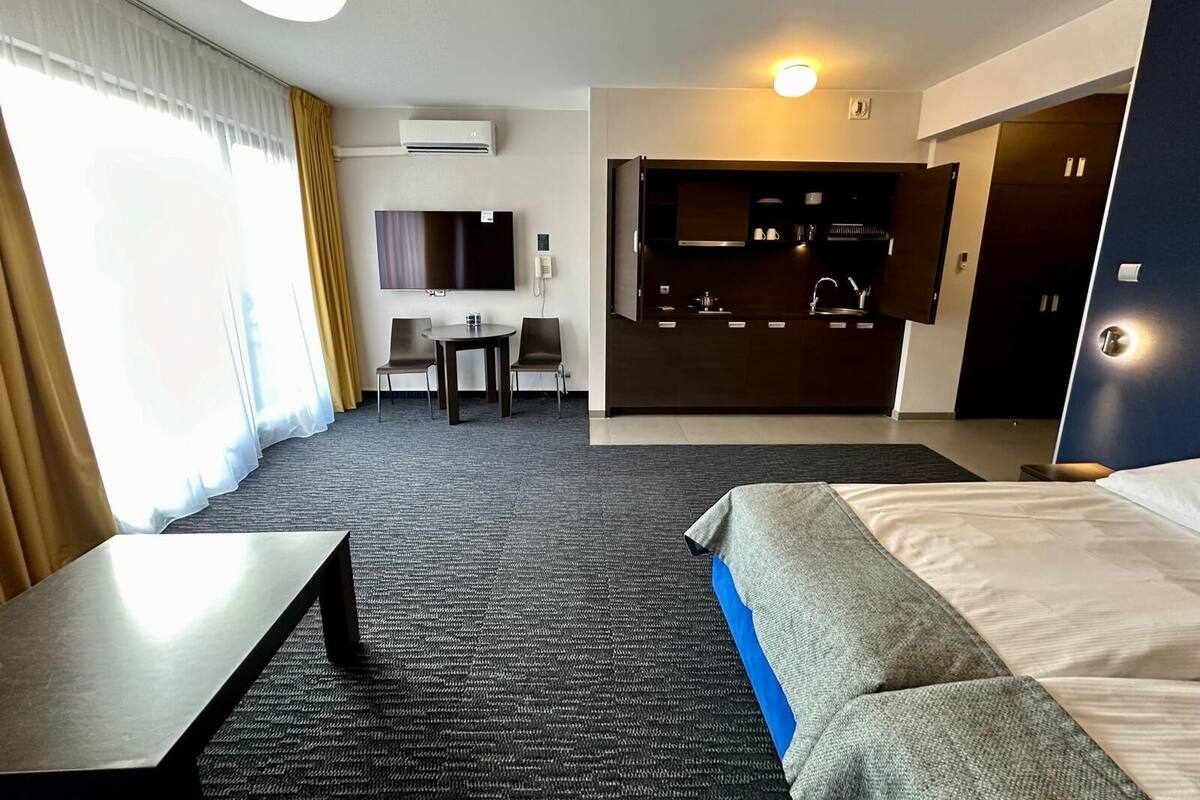 Ein Hotelzimmer mit Bett, Schreibtisch, Stuhl, kleinem Tisch, Fernseher, einer Küchenzeile und einem Badezimmer.