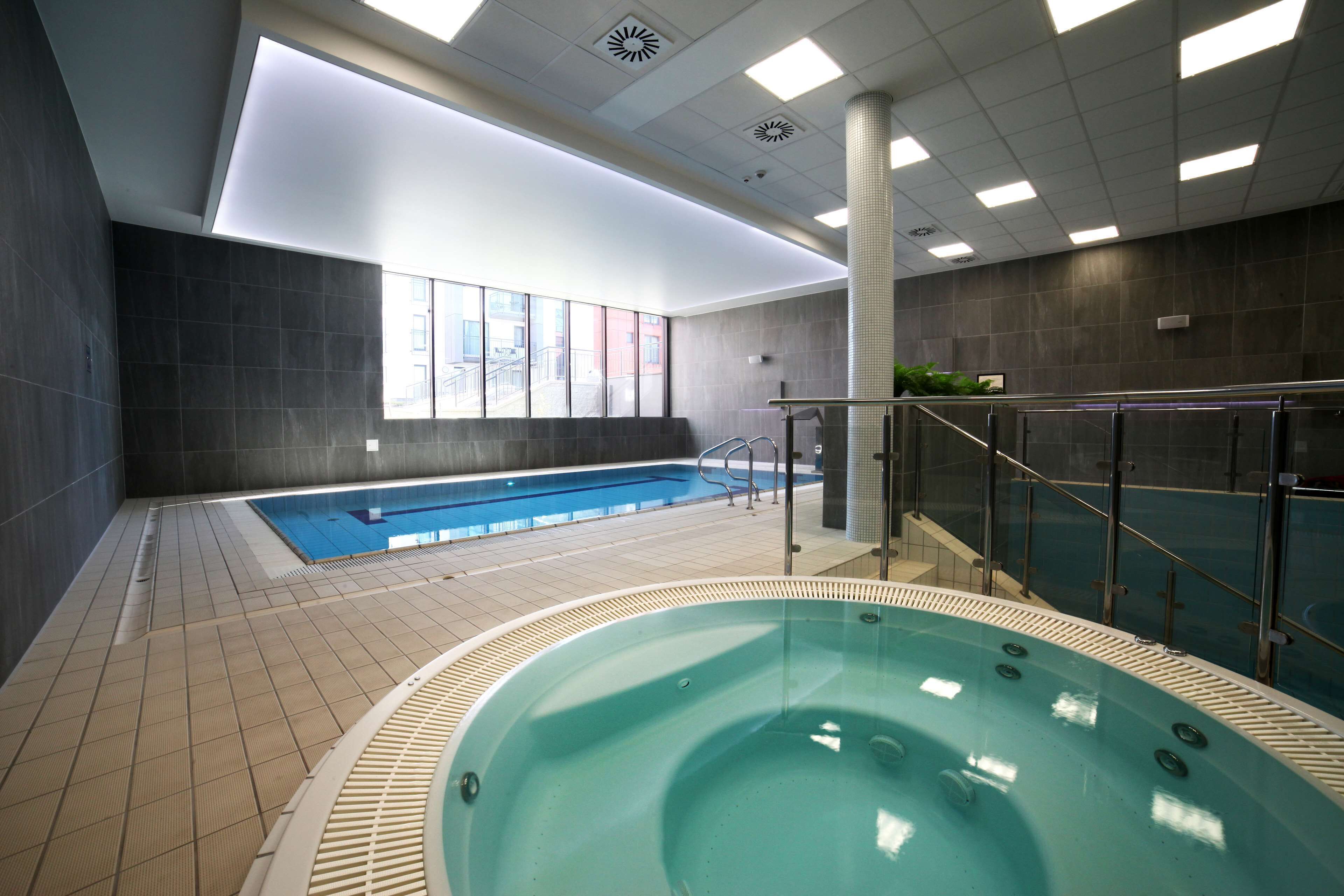 An indoor swimming pool with a separate hot tub area, tiled flooring, and a view of the outside through large windows.