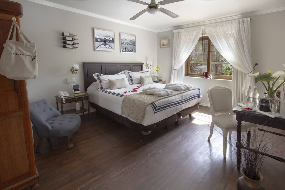 A neatly arranged bedroom with a bed, bedside tables, a chair, a desk, and a window with curtains.