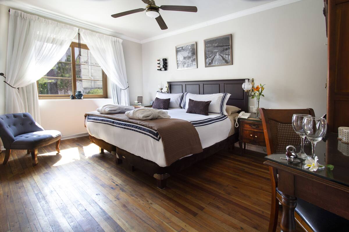 A bedroom with a bed, a chair, a desk, and a window with curtains.