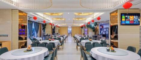 A dining area with round tables and chairs, a digital menu board, and a ceiling with circular light fixtures.