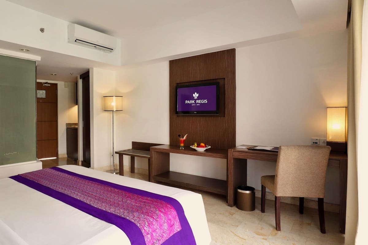 Une chambre d’hôtel avec un lit, un bureau, une chaise, une télévision et une petite table avec des fruits.