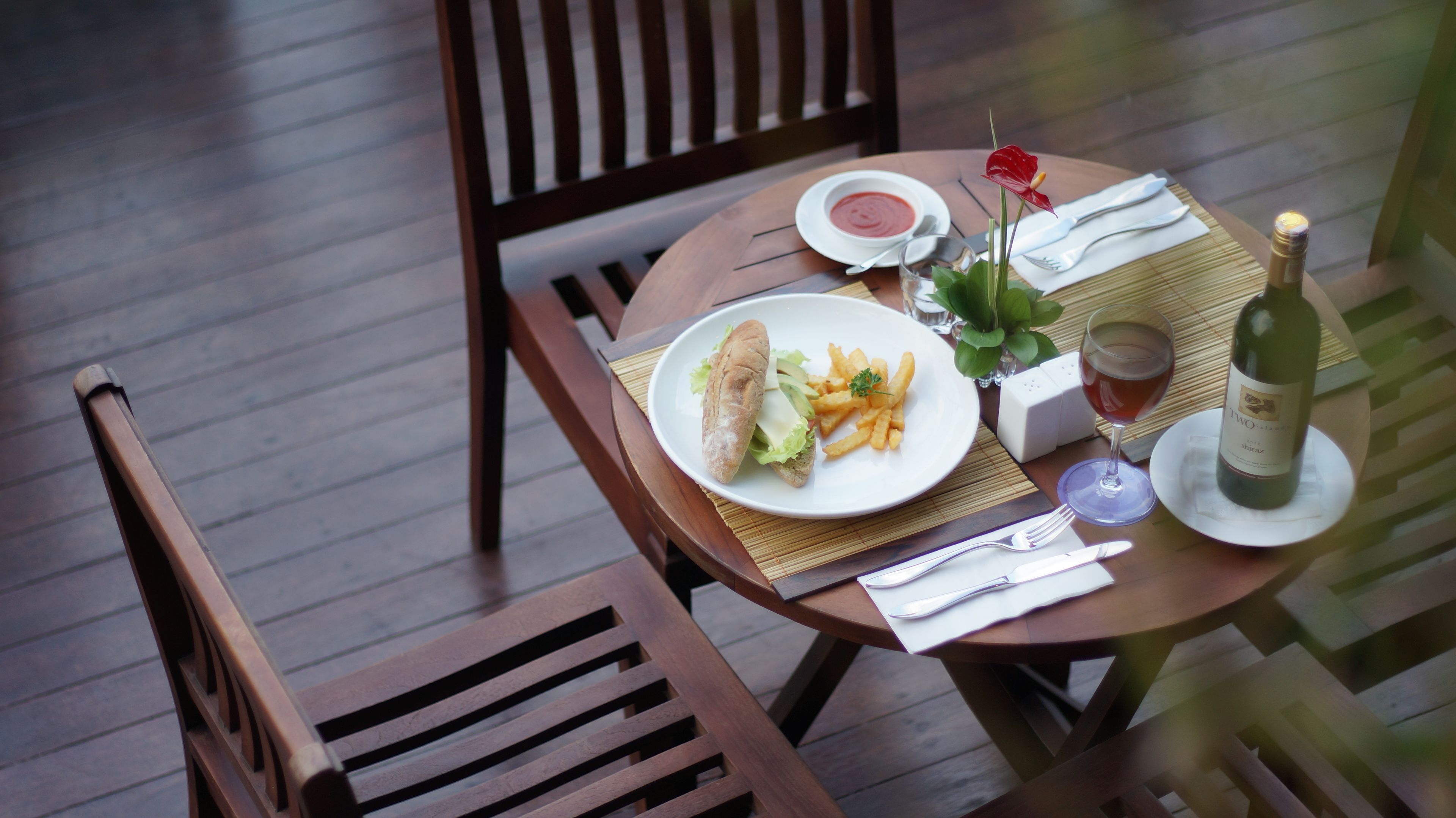 A table set with a sandwich, fries, a glass of wine, and a bottle of wine.