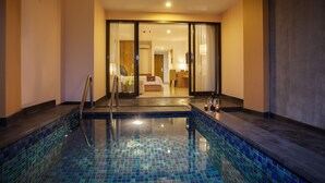 A hotel room with a large window, a bed, a bathroom, and a pool area with a glass barrier. - Park Regis Kuta, Bali (Kuta)