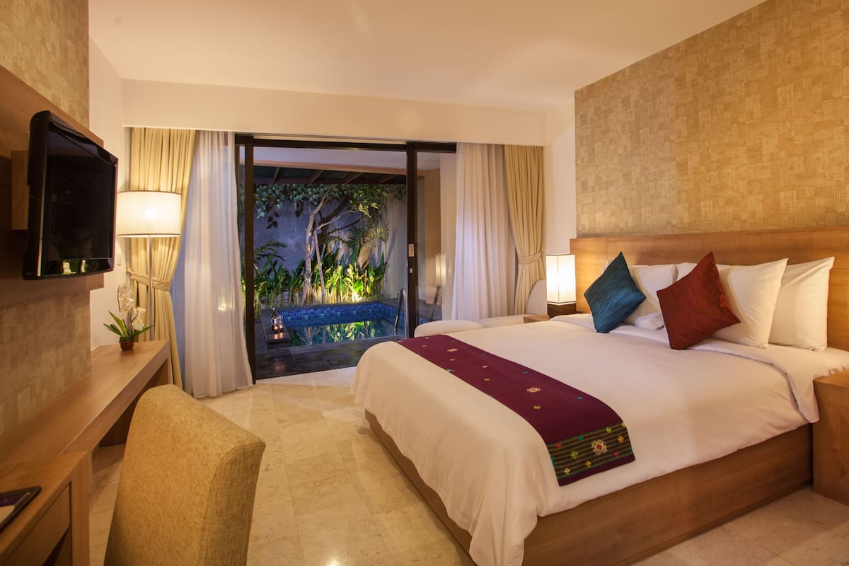 Une chambre d’hôtel avec un grand lit, un téléviseur fixé au mur, une table de chevet avec une lampe et une vue sur l’espace piscine.