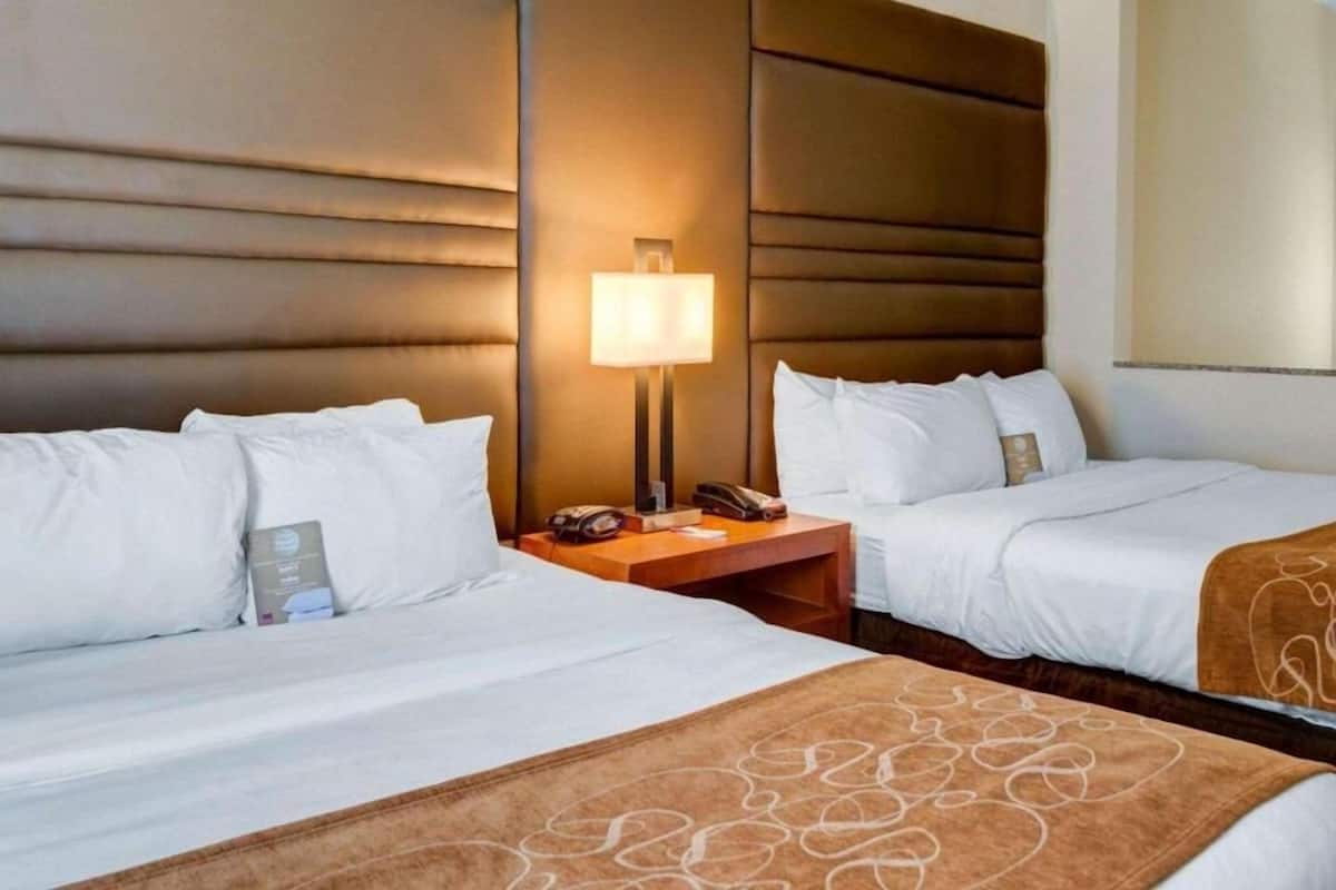 A hotel room with two beds, a nightstand with a lamp, and a large wall panel.