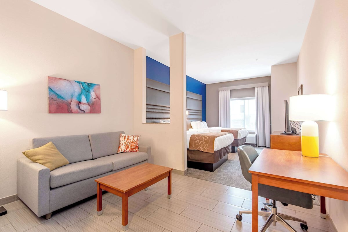 A hotel room with a sofa, a bed, a desk, and a painting on the wall.
